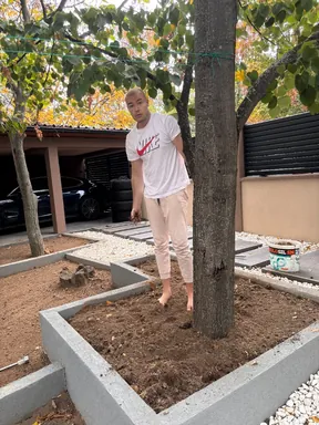 Marko Živić standing barefoot in a garden planter beside a tree